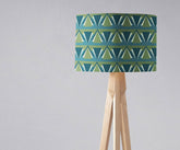 Cylindrical blue art deco lampshade with teal and olive triangles on a wooden tripod table lamp base