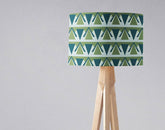 Green and grey art deco lampshade with geometric green and teal triangles on a wooden tripod table lamp base