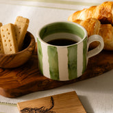 A large hand painted ceramic mug with green stripe pattern filled with dark coffee