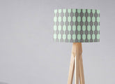 A mint green and gray geometric table lamp shade with a light wood tripod base and inch diameter design