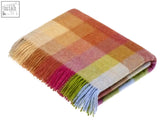A soft harlequin check pure new wool throw in warm sunshine tones with a cozy plaid pattern and fringed edges