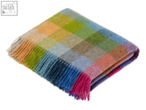 A soft folded pure new wool throw in tutti frutti harlequin check with vibrant plaid and fringed edges