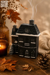Black haunted holiday house incense cone burner with white trim, faux shingles, and smoke rising from chimney