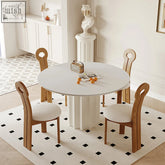 White round dining table with fluted pedestal base and minimalist wooden chairs with cream upholstered seats
