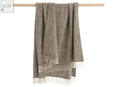 A soft herringbone natural undyed pure wool throw blanket in pale grey with cream fringe perfect for cozy use