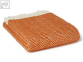 A folded cinnamon herringbone pure new wool throw blanket in orange and cream with white fringe