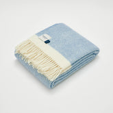 A soft dusk blue herringbone wool blanket with cream fringe and matching border perfect for cozying up