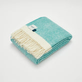 A folded herringbone wool blanket in turquoise and cream with a soft textured weave perfect for cozy warmth