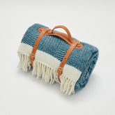 Teal and cream herringbone wool picnic blanket with tan leather straps and fringe perfect for outdoor use