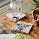 Two light gray natural limestone coasters with black ink deer and highland cow illustrations heat resistant