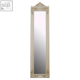 An ornate off-white holmes champagne floor mirror with intricate carved frame and decorative crest at the top
