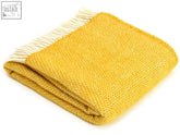 A folded honeycomb pure new wool throw blanket in golden yellow with cream fringe along one edge