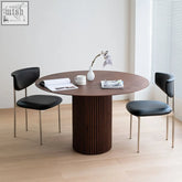 Round dark oak ivar round dining table with vertical ribbed base and minimalist black leather chairs
