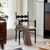 Black wooden jiro dining chair with wavy backrest and beige cushioned seat draped with taupe fringe scarf