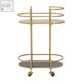 Gold-finished metal kobra trolley with two oval glass shelves and caster wheels for easy mobility, not a grey trolley