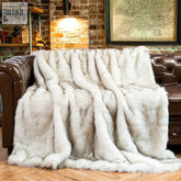 A plush light gray faux fur lagoto throw with soft luxurious texture draped over a brown leather couch