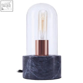 A sleek lamonte bell lamp with a clear glass dome, copper base, and black marble base pedestal