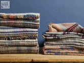 Stacks of large checked random recycled wool blankets in earthy tones with woven plaid patterns for cozy use