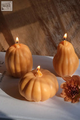 Three large orange pumpkin candles made from smooth soy wax with lit wicks adding seasonal charm