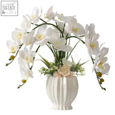 White ceramic vase with vertical ridges holds lesing artificial flowers ochids for indoor home decoration