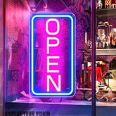 A vibrant neon open sign with bold white letters and a glowing blue frame on a pink background for business use