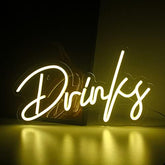 A glowing white warm white led neon sign that spells drinks in cursive for bar kitchen shop party decor