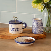 Cream-colored ceramic mug with blue speckles and navy rim hand painted with love and heart-shaped metal spoon