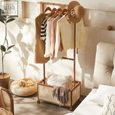 Wooden and rattan madeline coat rack with woven basket base holding pastel sweaters and a straw hat on top
