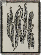 Beige woven magic beans blanket with black and white embroidered stylized curling bean pods and floral patterns
