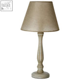 A beige textured fabric lampshade on a slender distressed white maine lined wooden candlestick table lamp base