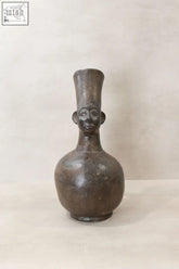 A dark matte mangbetu clay pot with a stylized human face and tall cylindrical neck from 20th century african art