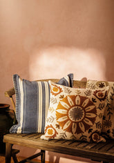 A beige margot striped cushion with embroidered floral patterns in brown orange and gray on a wooden bench