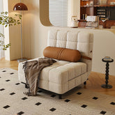 Beige striped tufted corduroy sofa bed with brown cylindrical pillow and patterned throw blanket draped over it