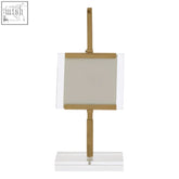 Gold-toned table lamp with a rectangular frosted glass shade and clear acrylic frame shown next to a small photo frame