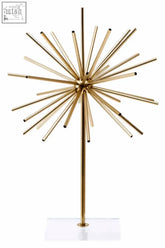 Milton metal sculpture is a gold metal sculpture with slender rods radiating from a hub on a clear acrylic stand