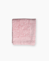 A soft pink cotton quilted blanket with delicate white botanical hand blocked printed design and striped border
