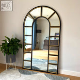 Arched window mirror with black and gold metal frame featuring multiple rectangular mirrored panels in a decorative grid