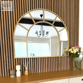 Gold metal arched window mirror with segmented glass panels and central reflective surface for stylish decor