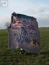 A gray wool mount lucio blanket with a textured feel and vibrant purple and red mountain landscape design