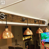Four copper dome pendant lights with black metal arms hang from rustic wood beam perfect for client area lighting
