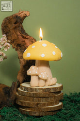 A yellow mushroom family candle with white polka dots and a lit wick featuring two smaller matching candles at the base