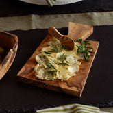 Rustic olive wood butter board with natural grain pattern featuring sliced cheese and fresh rosemary with wooden spoon