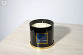 Black cylindrical large candle jar with gold trim and blue li home oud sapphire label containing three white wicks