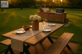 A rustic outdoor farmhouse dining table with black metal cross legs set with plates flowers and a pitcher
