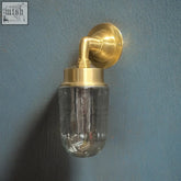 A clear glass soap dispenser with a solid brass swan neck wall light base and mounting bracket in brass finish