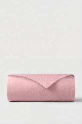 A soft pink linen percale duvet cover neatly rolled against a neutral background perfect for cozy bedding
