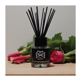 Black glass diffuser bottle with dank mer pink rhubarb label and black reed sticks featuring pink rhubarb fragrance oil