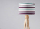 Purple striped lampshade with horizontal purple teal and white stripes on a light wood tripod table lamp base