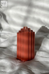 A terracotta pyramid sculpted candle with geometric segments and a central wick for home decor