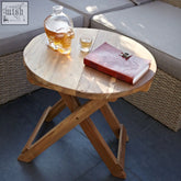 A clear glass skull decanter with amber liquid on a teak wood round folding coffee table 50x50cm